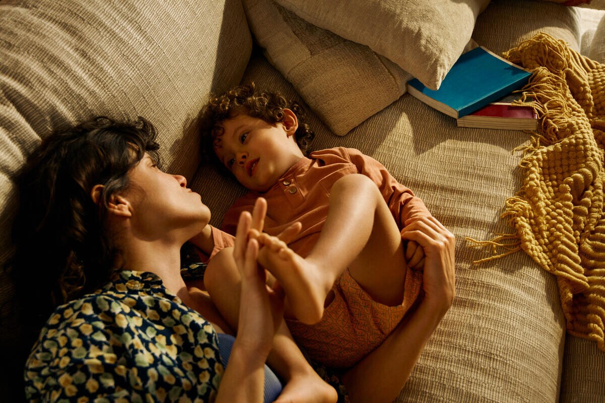 A mother and toddler cuddle on the couch together.